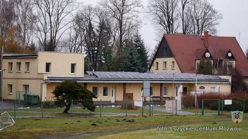 Zdjęcie przedstawia kremowy budynek socjalno-biurowy położony przy ul. Ludowej. Na dachu budynku zamontowano instalację fotowoltaiczną.